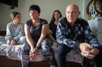 Ukrainian family, mother, father and two daughters sitting on a bed.