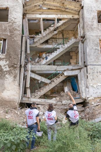 Mercy corps humanitarian workers in front of a damaged residential building