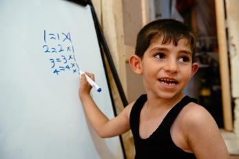 A young boy writing multiplication tables on a dry erase board