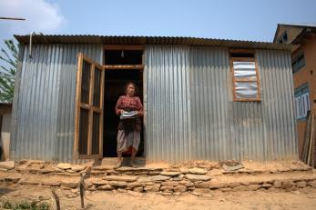 Nepalese woman in front of simple steel structure home.