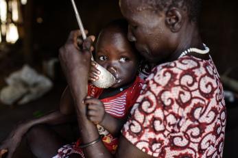 South sudanese woman feeding child with laddle