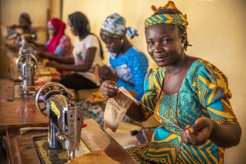 Nigerian woman producing textiles while seated at sewing machines.