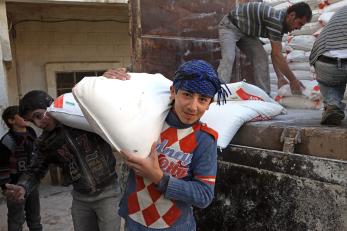 A boy carries a sack of flour over his shoulder in syria