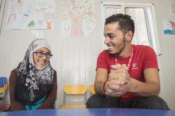 A mercy corps team member sits next to a girl, both smiling and talking, in jordan