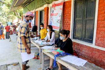 An adult waits while an aid worker completes paperwork on a table