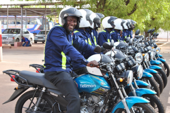 A group of motorcycle taxis and their drivers lineup in a row. 