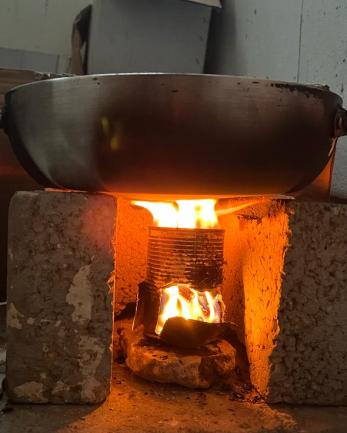 Cooking pot propped on bricks with can beneath heating with fire