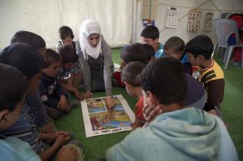 Children gathered around a woman who is leading the group in an activity