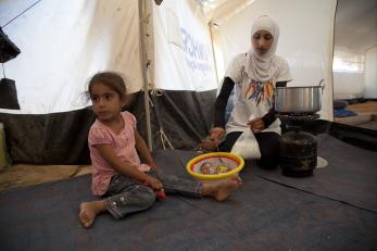 Syrian family members in refugee tent preparing a meal.