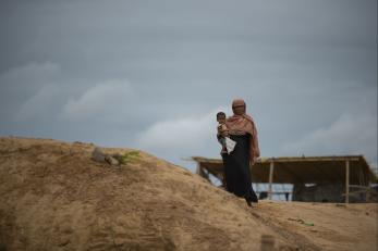 A Rohingya woman holds her child atop a hill as clouds bearing monsoon rains approach the world's largest refugee camp