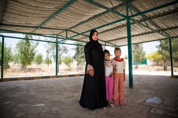 A woman stands beneath the shade of a shelter with her two young daughters