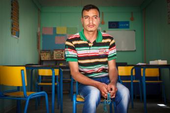 A man sitting in a classroom holding blue prayer beads