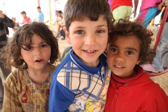 Three young children smile at Zaatari camp.