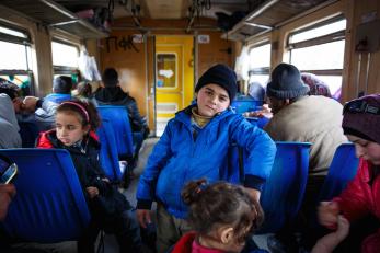A boy leans against a row of seats on a crowded train car