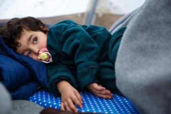 A young girl with a pacifier resting in a temporary shelter