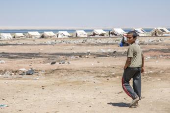 A boy walks toward a row of white tents in a dry, desert landscape