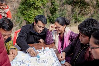 A group of people sit around a table and write on a large piece of paper in Nepal.