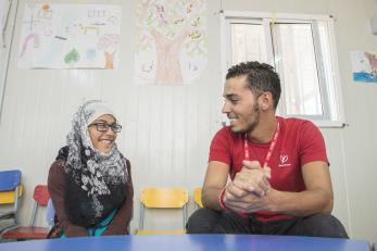 A Mercy Corps staff member sits at a table smiling with a young participant in Azraq, Jordan.