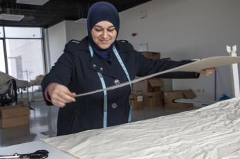 Jordanian woman measures textiles in workspace.