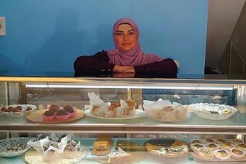 A business owner leaning on a display case of baked goods.