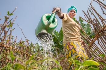 Woman in DRC watering crops with a watering can.