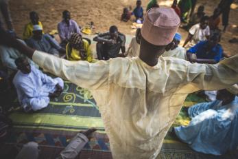 Nigerian man stands above community members he's speaking with.