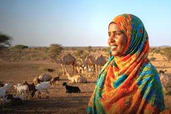 Woman smiling, overlooking pastoral land with livestock in the background.