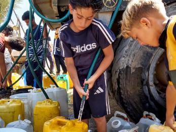 Young Palestinian children filling jerrycans with potable water.