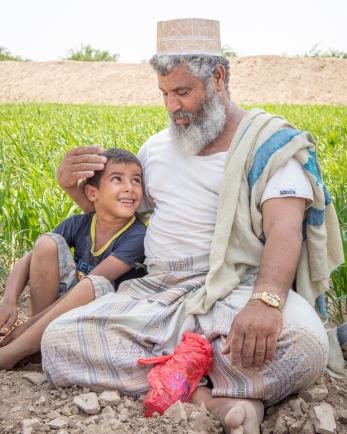 A farmer and his grandson smile at each other in a field in Yemen. 