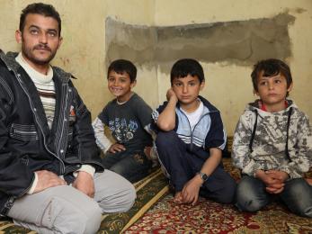 Abid, who fled to lebanon from syria one year ago, sits with four of his eight children in the cowshed they're now forced to call home.