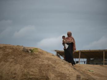 A rohingya woman holds her child atop a hill as clouds bearing monsoon rains approach the world's largest refugee camp