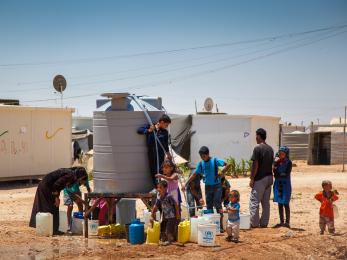 Families get water from a tank at a refugee camp