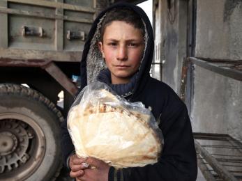 A boy wearing a black hooded sweatshirt holds bread in syria