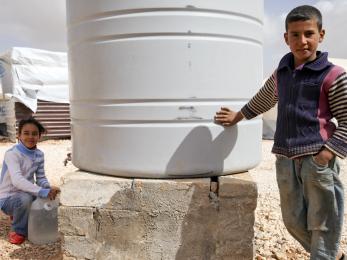 A girl and boy next to a large white water tank at a refugee camp in jordan