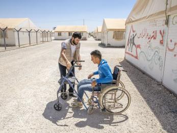 A mercy corps team member works with a young man who uses mobility equipment at a refugee camp in jordan
