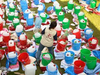 A mercy corps team member standing among buckets filled with emergency supplies in nepal