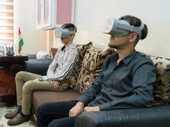 Two young participants in iraq wear virtual reality goggles which provide visual and audial immersion.