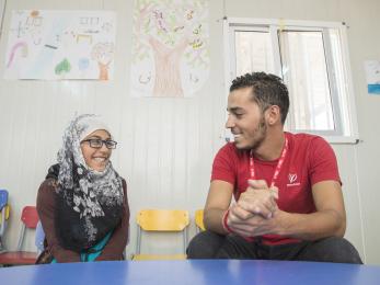 A mercy corps staff member sits at a table smiling with a young participant in azraq, jordan.