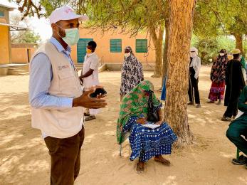 Participants in tillaberi region, niger, listen to a mercy corps representative wearing a facemask explaining details about a program.