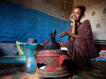 An adult sits and waits for coffee to brew inside her home in ethiopia