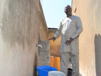 A person standing next to a tap in their compound connected to the local water facility.