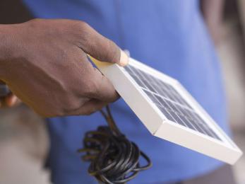 A hand holding a solar panel with a power chord hanging from it.