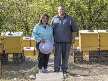 Ukrainian woman and man stand among bee hives.