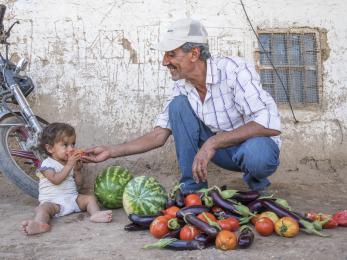 Man and baby with vegetables and fruit on the ground between them