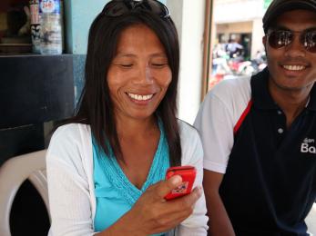 A woman smiles while holding her phone and making a mobile banking transaction.