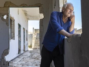 Syrian man standing in outdoor hallway, smiling.