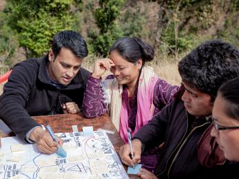 A group of people sit around a table and write on a large piece of paper in nepal.