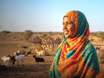 Woman smiling, overlooking pastoral land with livestock in the background.